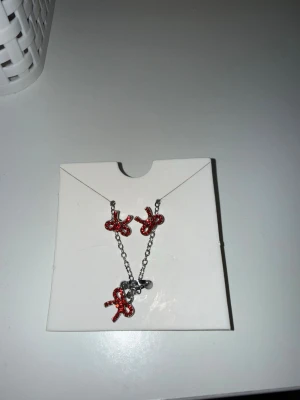 Silverfärgat halsband och örhängen med röda pärlor - Snyggt halsband och örhängen i silverfärg med tre röda dekorationer formade som rosetter, täckta av små pärlor. Kedjan är tunn. Perfekt accessoar för att ge din outfit en färgklick.