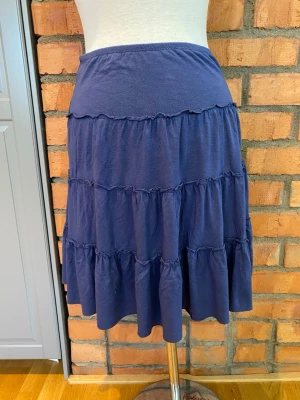 Bik bok Blå volangkjol i bomull strl M - Mjuk och skön blå kjol med flera volanger och bred midjeresår. Kjolen har en avslappnad passform och är tillverkad i rayon, vilket gör den perfekt för varma dagar. Enkel att matcha med olika toppar för en trendig look.