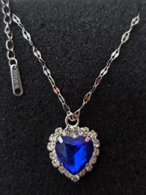  💎 TITANIC ”HEART OF THE OCEAN” – ROSTFRITT STÅL 💎 - Dröm dig bort till filmens värld med detta fantastiska ”Heart of the Ocean”-inspirerade halsband! En djup safirblå kristall formad som ett hjärta, omgiven av glittrande strass-stenar som verkligen fångar ljuset. Halsbandet är både elegant och tidlöst – en perfekt present eller ett statement-smycke till festen! ✨ Detaljer: Material: Rostfritt stål (Stainless Steel / S-STEEL) – tål vatten, mörknar inte och är snällt mot huden. 💧 Design: Klassisk replika inspirerad av Titanic. Skick: Helt nytt! 🌟
