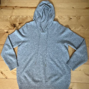 Ljusgrå hoodie i merinoull - Mysig ljusgrå hoodie med huva och dragsko. Tillverkad i mjukt stickat material som känns skönt mot huden. Hoodien har ribbade muddar vid ärmslut och nederkant för en avslappnad look. Perfekt för chill dagar eller när du vill vara extra bekväm.