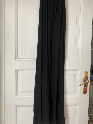 Svart långklänning med tunna axelband - En svart långklänning med tunna axelband, lite djupare i ryggen (se bild 3) och lätt rynkad struktur. Klänningen har en enkel, flowy passform och är tillverkad i ett tunt, mjukt tyg som ger en avslappnad känsla. Perfekt för varma dagar eller att styla upp med accessoarer.