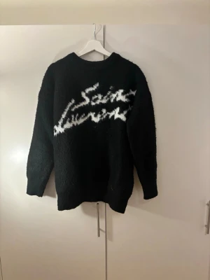 Svart stickad Saint Laurent tröja - Svart stickad tröja från Saint Laurent med vit logga i graffiti-stil över bröstet. Tröjan är helt oanvänd pga av storlek, skriv vid funderingar