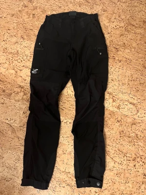 Svarta friluftsbyxor RevolutionRace - Säljer ett par svarta friluftsbyxor från RevolutionRace då dem är förstorar för mig, har använt dem men sparsamt. Som man kan se på ena bilden har färgen på knapparna, på båda benen vid fötterna släppt lite på. Då dem tvättades i lite hög grad. Annars i fint skick! Köparen står för frakt! Kan även byta byxorna till storlek 34/xs! Hör av er vid frågor☺️