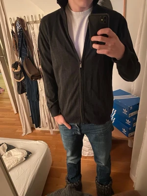 Mörkgrå ziptröja från Reserved - Säljer en fet ziptröja från Reserved i mjuk bomull. Tröjan har hög krage, dragkedja framtill och ribbade muddar vid ärmslut och nederkant. Enkel och stilren design som passar till det mesta.