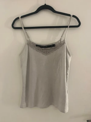 Beige linnetopp med spetsdetalj - Säljer en vit linnetopp från lager 157 med tunna axelband och fin spetsdetalj vid urringningen. Toppen har en enkel och stilren design som passar perfekt till sommaren. Materialet känns mjukt och lätt mot huden.