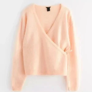 Ljusrosa omlottkofta - Mysig ljusrosa omlottkofta med långa ärmar och knytband i sidan. Koftan har en djup V-ringning och är tillverkad i ett mjukt, fluffigt material som ger en avslappnad och trendig look.