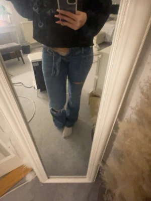 Blå ripped jeans från Gina Tricot - Säljer ett par blå jeans från Gina Tricot i storlek XS. Jeansen har slitningar vid knäna och en avslappnad passform med bootcut ben. Klassisk femficksmodell och tillverkade i denim. Perfekta för en trendig och avslappnad look.