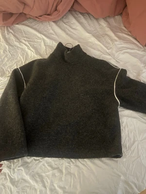 Mörkgrå polo stickad tröja - Mörkgrå croppad stickad tröja med hög krage och vita kontrastsömmar längs axlarna. Tröjan har en boxig passform och långa ärmar. Perfekt för lager på lager och en chill look.