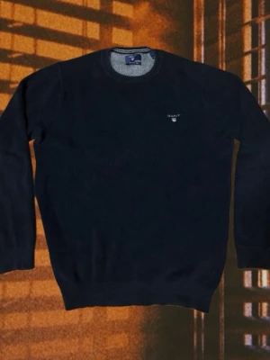 Mörkblå tröja från Gant - Klassisk mörkblå rundhalsad tröja från Gant med diskret logga broderad på bröstet. Tröjan har ribbade muddar vid ärmslut och nederkant samt är tillverkad i mjukt stickat material. Perfekt för en stilren och enkel look.