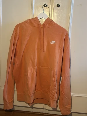 Nike hoodie i orange - Säljer en snygg hoodie från Nike i en unik rostorange färg. Hoodien har klassisk huva med dragsko, stor magficka och Nike-logga broderad i vitt på bröstet. Tillverkad i mjukt bomullsmaterial som är skönt mot huden. Perfekt för en avslappnad streetwear-look.