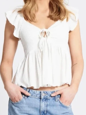 Vit volangblus med knytning - Söt vit blus med volangärmar och knytning framtill. Blusen har en luftig, rynkad struktur och lätt v-ringad hals. Tillverkad i ett tunt, mjukt tyg som ger en flowy känsla. Perfekt för en somrig och avslappnad look🤍