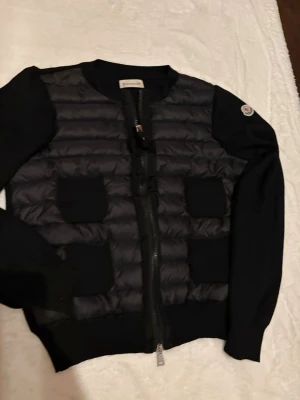 Moncler quiltad cardigan dam - Snygg och trendig cardigan med quiltad framsida och stickade ärmar. Storlek 1, passar xs/s dam   Inköpt på vinted med tilläggstjänsten äkthetsverifikation, qr-kod finns även.  I Mycket gott skick!  Nypris 10.000:-