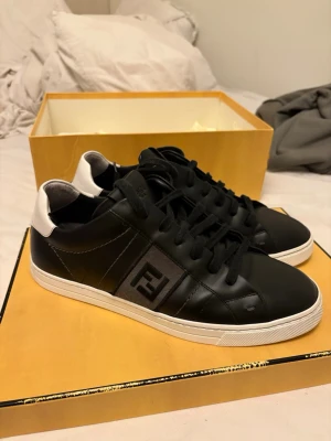 Svarta Fendi sneakers med vit häl - svarta sneakers från Fendi med vit detalj på hälen och klassisk Fendi-logga på sidan. Superbra skick  tecken på användning finns (se bilder) bland annat insida häl och innersula låda och dustbag etc finns
