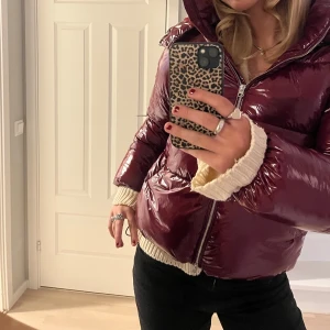 Nelly vinröd pufferjacka  - Säljer en glansig vinröd pufferjacka med huva och dragkedja framtill. Jättesnygg och varm. Säljer pga ej kommer till användning, men endast använd fåtal gånger💕