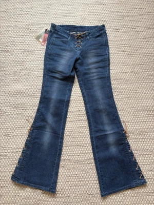 Jeans med knytdetaljer - Så coola lågmidjade jeans med knytdetaljer vid gylfen och på båda benen. Midjemått: 36 cm mätt rakt över. Innerbenslängd: 80cm. Storlek 25, skulle säga att den passar en XS. Prislappen kvar. 