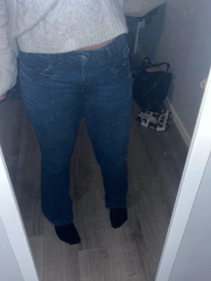 Blå bootcut jeans med låg midja - Säljer ett par klassiska blå bootcut jeans med låg midja och fem fickor. Jeansen har en snygg tvätt och är tillverkade i ett stretchigt denim-material som sitter bekvämt. Perfekt för dig som gillar retrovibbar och vill ha ett par jeans med lite utsvängda ben. Storlek 164 men passar mig som har storlek S i vanliga fall