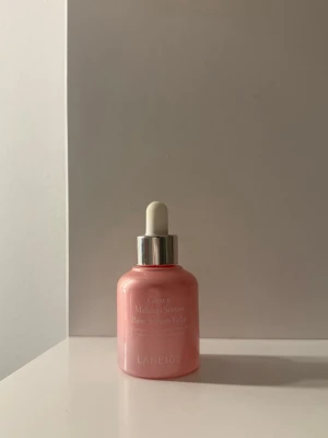 Laneige Glowy Makeup Serum Primer - Primer i serumform från Laneige med en glansig, rosa flaska och pipettapplikator i vitt och silver. Ger huden en fräsch och återfuktad känsla, perfekt som bas innan smink. Snygg och modern design som passar på sminkbordet.