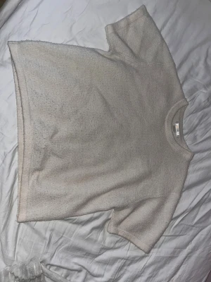 Beige stickad kortärmad  - En ljusbeige stickad topp med korta ärmar och rund hals. Toppen har en loose passform och är tillverkad i ett tunt, luftigt material som passar perfekt till varma dagar. Enkel och stilren design som är lätt att matcha.