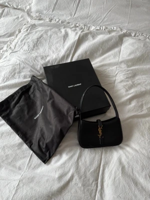  Saint Laurent axelväska - Säljer min fina YSL väska, svart slätt läder med guld logga, storlek mini, väldigt fint skick och kvitto finns 