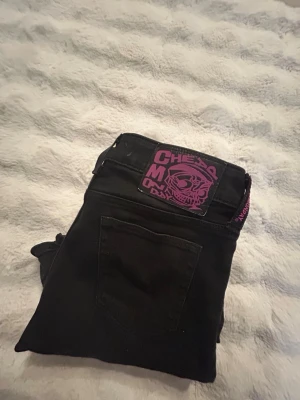 Svarta Cheap Monday jeans - Säljer ett par svarta jeans ifrån Cheap Monday med ett rosa tryck på baksidan. Står tyvärr inte storlek men skulle kunna tro 26-32. Stretchigt material och bara andvända ett par gånger 🤩