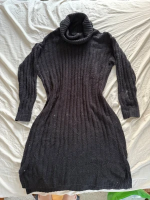 Svart stickad poloklänning från Lager 157 - Mysig svart stickad klänning med polokrage och lång ärm. Klänningen har ribbstickat mönster och är figurnära i modellen. Perfekt för kyliga dagar och enkel att styla med boots eller sneakers. De små vita prickarna är katt hår som har fastnat, det går att få bort. Annars har den inga fläckar och inga hål