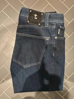 Mörkblå jeans från Tramarossa - Snygga mörkblå jeans från Trammarossa. Jeansen har en unik patch bak som är avtagbar och detaljerad brodyr på insidan. Tillverkade i mjukt denimtyg för en bekväm känsla. Hör av er vid frågor! Skulle säga att de passar W 30-32 och L 32-34