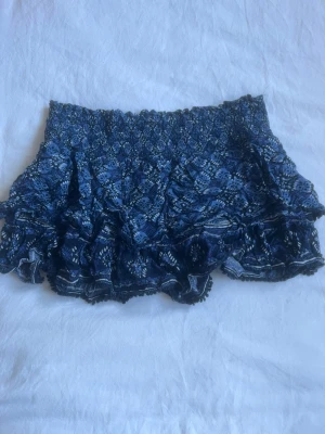 Blå volangkjol från Superdry - Supersnygg blå kjol från Superdry med volangdetaljer och smockad midja. Mönstrade i olika blå toner och vita inslag, perfekta för sommarens alla äventyr. Lätta och luftiga med en loose passform och elastisk midja för extra komfort. Og pris 600kr. 