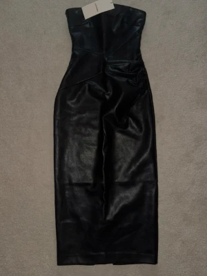 Svart axelbandslös klänning Adoore - Säljer en svart, axelbandslös långklänning i läder som ger en cool och edgy look. Klänningen har en figurnära passform och är perfekt för dig som vill sticka ut. 