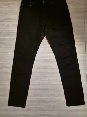 Svarta raka jeans från Levi's - Säljer ett par svarta jeans från Levi's med klassisk rak passform och fem fickor. Jeansen har Levi's röda etikett på bakfickan och är tillverkade i ett slitstarkt denimtyg. Perfekta för en clean och stilren look. Storleken är W30 L30 och modellen är 512. 