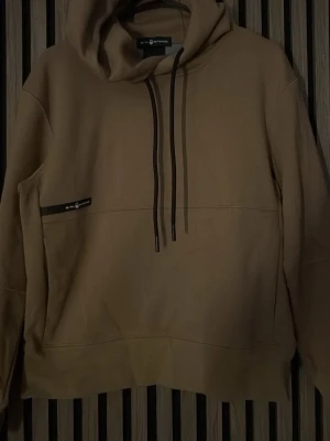 Brun hoodie från Sail Racing - Säljer en oandvänd brun hoodie från Sail Racing i storlek Small. Hoodien har en stor huva med svarta dragsnören och en ficka framtill med en liten Sail Racing-logga. Tillverkad i mjukt bomullsmaterial som känns skönt mot huden.