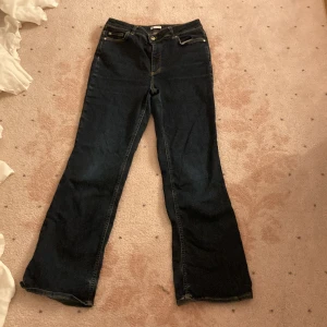 Mörkblå bootcut jeans med fickor - Säljer ett par low waist mörkblå bootcut jeans med klassiska fem fickor och kontrastsömmar. Jeansen har normal midja och utsvängda ben, perfekta för en avslappnad och trendig look. Materialet är denim i bomull med lite stretch för extra komfort. 