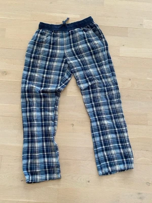 Rutiga blåa flanellbyxor - Mysiga loungewear-byxor i blått och vitt rutigt flanelltyg. Byxorna har resår och dragsko i midjan samt raka ben. Perfekta för chill hemma eller som pyjamasbyxor.
