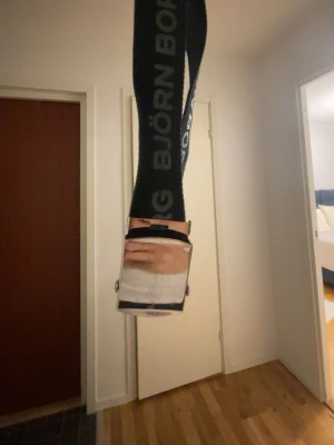 Svart Björn Borg bälte med silverdetalj - Snyggt svart bälte från Björn Borg med tydlig logga längs hela bandet. Bältet har ett stilrent spänne i silverfärgad metall och är gjort i ett slitstarkt syntetmaterial. Perfekt accessoar för att lyfta din outfit.