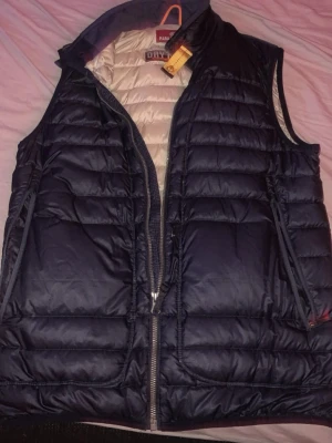 Mörkblå dunväst från Parajumpers - Snygg mörkblå dunväst från Parajumpers med quiltad design och dragkedja framtill. Insidan är ljusbeige och västen har hög krage samt praktiska fickor. Perfekt för lager på lager och ger en sportig look.