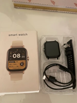 Svart fyrkantig smartklocka - Snygg svart smartklocka med fyrkantig display och silikonarmband. Klockan har en modern design och levereras med laddningskabel. Perfekt för att hålla koll på steg, tid och notiser direkt på handleden.💕