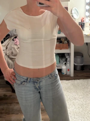 Vit croppad topp med kort ärm - Snygg vit croppad topp med korta ärmar och rund halsringning. Toppens material är stretchigt och sitter tight mot kroppen, perfekt för en trendig och enkel look. Passar till både jeans och kjol.