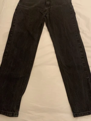 Svarta raka jeans - Säljer ett par svarta jeans med rak passform och hög midja. Jeansen har klassisk femficksdesign och är tillverkade i denim. Perfekta för dig som gillar en enkel och stilren look. Storlek 27