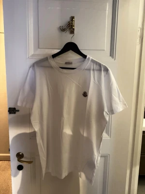 Vit t-shirt från Moncler - Säljer en klassisk vit t-shirt från Moncler med korta ärmar och rund hals. Kolla min profil, säljer även likadana T-shirts i grått och svart. Storlek M, herr. Skriv om du vill köpa alla tre T-shirts för ett pris på sammanlagt 1750kr