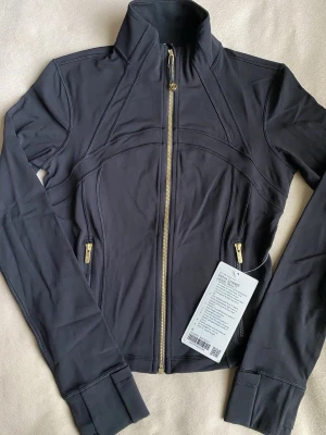 Lululemon Define Jacket XS (6) – Figurnära träningsjacka - • Storlek: XS / 6 • Modell: Define • Stretchigt och bekvämt material • Figursydd passform • Dragkedja framtill • Praktiska fickor  Kan även köpas tillsammans med matchande byxor (säljs separat eller som set).  Plagget är i fint skick. Hör gärna av dig om du vill ha fler bilder eller mått.