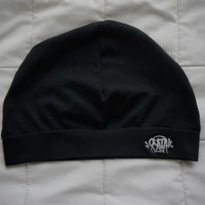 Syns Skullcap - Säljer en svart mössa i mjukt bomullsmaterial med en broderad vit logga framtill. Mössan har en enkel och stilren design som passar perfekt till streetwear och vardagsoutfits. Flera kändisar som Marlon och Central Cee använder denna konstant! 