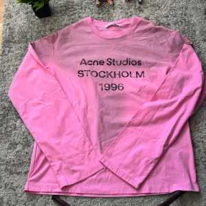 Rosa långärmad topp Acne Studios - Cool rosa långärmad topp från Acne Studios med tryck 'Acne Studios STOCKHOLM 1996' på bröstet. Tillverkad i mjuk bomull och har en relaxed fit. Perfekt för dig som gillar streetwear och vill sticka ut med färg.