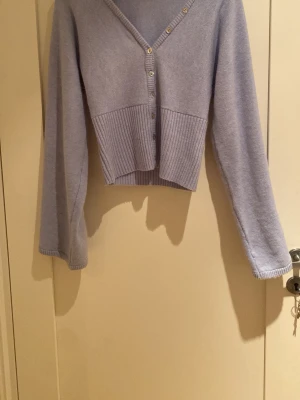 Ljusblå kofta med knappar - Kort, ljusblå kofta från Gina Tricot med v-ringning och dekorativa silverfärgade knappar framtill. Koftan har långa ärmar och bred ribbstickad nederkant. Säljer tröjan efter som jag köpte den i för stor storlek och ångrar mitt köp. Har bara använt tröjan 1 gång.
