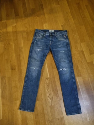 Feta replay jeans  - Säljer ett par blå jeans från Replay med slitningar och detaljer på benen. Jeansen har klassisk femficksdesign, raka ben och snyggt tvättad look. Perfekta för dig som gillar en avslappnad och trendig stil. Storlek 31/32