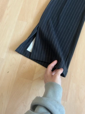 Mörkblå randiga kostymbyxor - Snygga mörkblå kostymbyxor med tunna vita kritstrecksränder och slits vid benslutet. Byxorna har rak passform och är tillverkade i ett klassiskt kostymtyg som känns dressat men ändå chill.