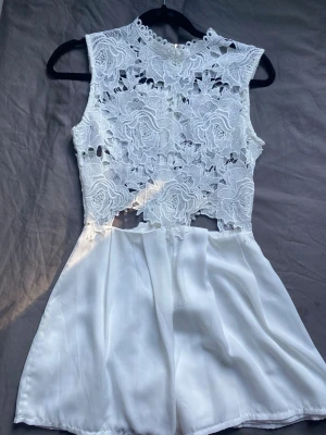 Vit spetsklänning med blommönster - Hej! Säljer denna vita jumpsuit/klänning i spets. Det ser ut som en klänning men är egentligen shorts nedtill vilket gör att man alltid känna sig bekväm. Märket är Passion Fusion och storleken är S. Den är aldrig använd och är därför i mycket bra skick samt inga defekter. ❣️