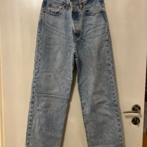 Ljusblåa jeans-Levis - Ljusblåa jeans från Levis i modellen Ribcage Straight. High waisted jeans med knappgylf och bitdekor. Skicket är mycket bra. Storleken är: W25, originalländgen är L29, men jeansen är uppsprättade så de är nog cirka 2,5 cm längre.