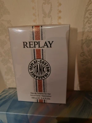 Replay # Tank Custom For Her Edt 100ml - Oöppnad, fortfarande inslagen i sitt plastomslag. 100ml.     , #TANK CUSTOM FOR HER ger en känsla av energi varje dag. Doften är ett dolt möte mellan förförisk honung och en elegant blombukett. En explosion av femininitet som berusar sinnena. Basen är en magnetisk omfamning av sensuell Patchouli, varm vanilj och exklusiv Orcanox.  Toppnoter: Honung, Sorbet, Äpple, Petitgrain Hjärtnoter: Apelsinblomma, Jasmin, Liljekonvalj Basnoter: Vanilj, Ambroxan, Patchouli  