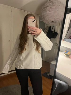 Vit kabelstickad tröja - Vit kabelstickad tröja med breda ärmar och rund hals. Tröjan har ett klassiskt flätmönster framtill och är gjord i ett mjukt, tjockt material som passar perfekt för kyligare dagar. Enkel att matcha med olika outfits.