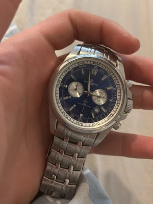 Jacques Lemans blå kronografklocka - Snygg kronografklocka från Jacques Lemans med blå urtavla, silverfärgade detaljer och datumvisning. Klockan har en robust länkarmband i rostfritt stål och flera funktioner på urtavlan. Perfekt accessoar för dig som gillar stilrena och sportiga klockor.