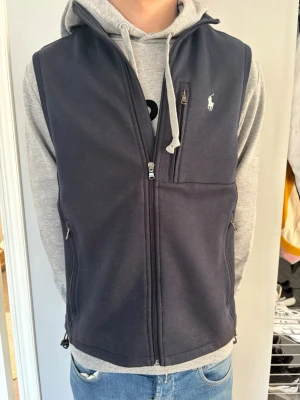 Mörkblå väst från Ralph Lauren - !PRIS KAN DISKUTERAS!  Snygg mörkblå väst från Ralph Lauren med dragkedja framtill och två sidofickor med dragkedja. Västen har en klassisk passform och är dekorerad med den ikoniska vita logotypen på bröstet. Perfekt att slänga över en hoodie för en casual look. 